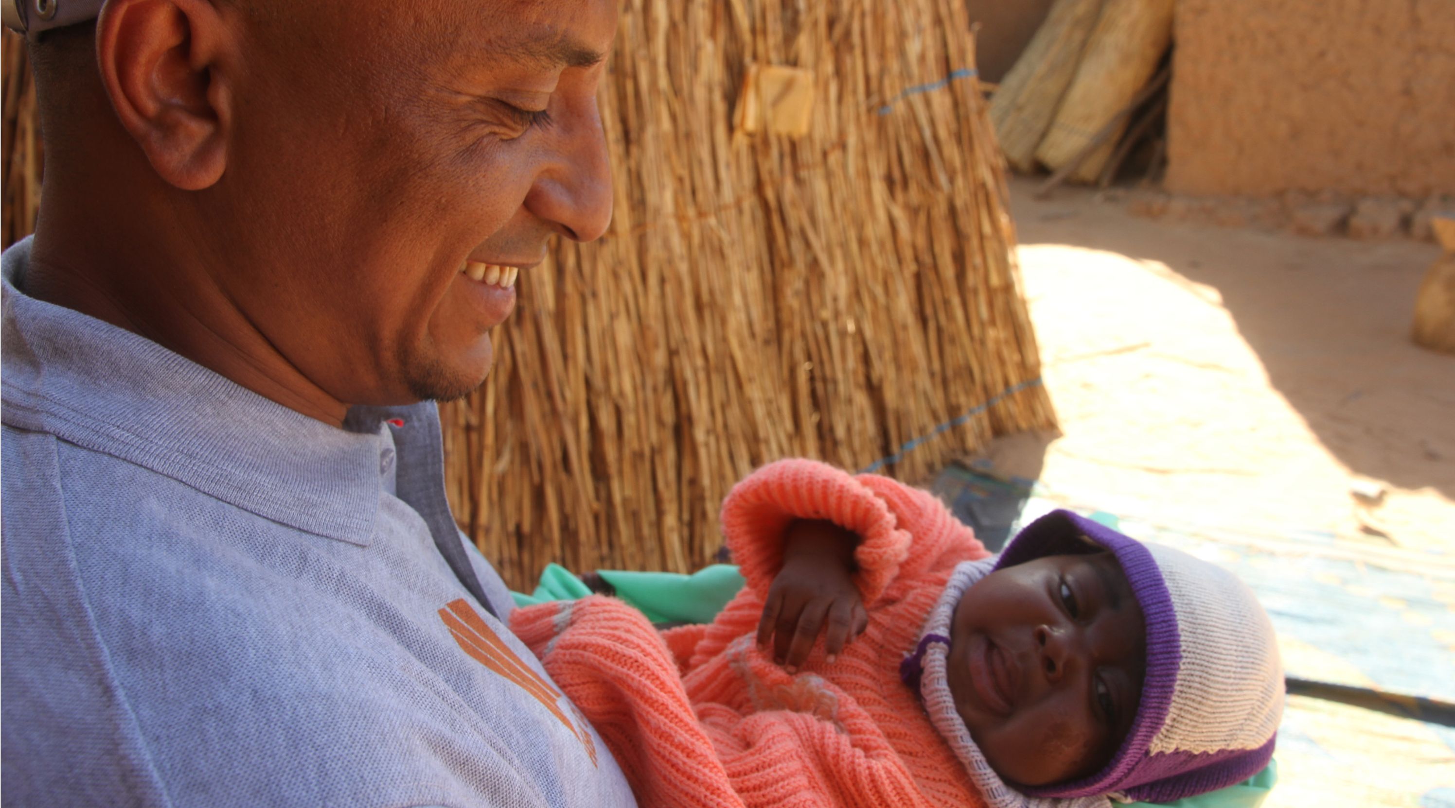 A child in a colorful outfit, smiling and sitting on a hospital bed.